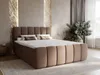 A bedroom scene with a large, upholstered boxspring bed as the focal point, decorated with pillows and a throw. The room features textured walls, curtains, and a plant. Produktbild-Vorschau