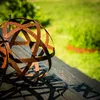 A rusty metal sphere sits on a wooden surface in a garden setting. Voir les images du produit
