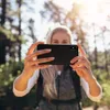 A woman is taking a selfie in a forest with a phone. Produktbild-Vorschau