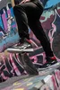 A person wearing black pants and Reebok high-top sneakers is balancing on a piece of wood in front of a graffiti-covered wall. Náhľad obrázku produktu