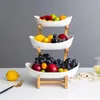 A three-tiered fruit stand filled with various fruits, placed on a white surface with a grey background. Náhled obrázku produktu