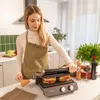 A woman is using an electric grill in a kitchen setting. Voir les images du produit