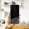 A hand holding a smartphone with a glittery black case. Produktbild-Vorschau