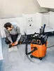 A man is using a power tool connected to a vacuum cleaner on a tiled floor, with kitchen cabinets in the background. Anteprima dell’immagine prodotto