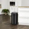 A black sensor trash can is placed on a dark wooden floor in a modern kitchen. Produktbild-Vorschau