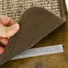 A hand is holding up a corner of a carpeted cat climbing structure, revealing a velcro strip attached to the underside of the carpet and a matching velcro strip on a wooden surface. Produktbild-Vorschau