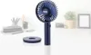 A navy blue portable fan and its charging base are displayed on a white surface, with a blurred background of office desk items. Anteprima dell’immagine prodotto
