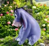 A purple Eeyore figurine sitting in a garden with flowers. Produktbild-Vorschau
