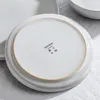 The underside of a speckled white ceramic plate with a tan rim, showing brand and care symbols. Produktbild-Vorschau