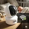 A baby monitor camera is placed on a wooden table next to a sleeping baby in a crib. A Wi-Fi signal icon with a cross indicates a connection issue. Náhled obrázku produktu