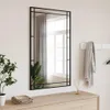 A rectangular mirror with a black frame hangs on a wall above a wooden dresser. A plant is on the left, and a scarf is draped over a coat rack on the right. Voir les images du produit
