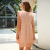 Frau in einem pfirsichfarbenen Rüschenärmelkleid, von hinten gesehen, über die Schulter blickend Produktbild-Vorschau