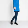 A person wearing a blue coat and dark jeans, standing and showing their feet in black shoes. Produktbild-Vorschau