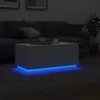 A white coffee table with blue LED lights is placed on a gray rug in a dimly lit living room, with a sofa in the background. Náhled obrázku produktu