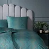 A close-up view of a bed with teal and gold patterned bedding and a grey headboard. Produktbild-Vorschau