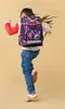 A young girl is jumping with a backpack on her back. Produktbild-Vorschau