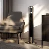 A modern tower fan is placed next to a chair and a dresser in a room with natural light. Podgląd zdjęcia produktu