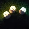 Three small, egg-shaped night lights with chick faces are placed on a grassy surface in the dark. Produktbild-Vorschau