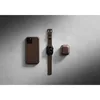 A brown leather iPhone case, a brown leather Apple Watch band, and a brown leather AirPods case are arranged on a textured gray surface. Podgląd zdjęcia produktu