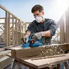 A man is using a Bosch power planer on a piece of wood, with construction framing in the background. Podgląd zdjęcia produktu