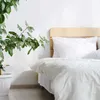 A bed with white bedding and a wooden headboard, next to a potted plant. Produktbild-Vorschau