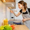 A woman cooking in a modern kitchen, tasting food from a spoon. Náhľad obrázku produktu