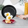 A hand is holding a frying pan with fried eggs over a plate of toast. Produktbild-Vorschau