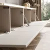 A close-up view of a white wall-mounted cabinet with its doors open, revealing internal compartments and hydraulic hinges. The cabinet is mounted on a wooden floor, and a window with curtains is visible in the background. Produktbild-Vorschau