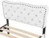 Close-up view of a white upholstered headboard with tufted buttons and nailhead trim, attached to a bed frame. Podgląd zdjęcia produktu