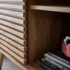 A close-up view of a wooden sideboard with a slatted front and a shelf inside, showing some books and a red bowl with white beads. Anteprima dell’immagine prodotto