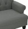 Close-up of a gray upholstered sofa or chaise lounge, showing the armrest and seat cushion. The sofa has tufted detailing on the backrest. A dark wooden leg is partially visible at the bottom right. Produktbild-Vorschau