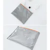 Two images of a gray cosmetic bag with an orange zipper, shown flat on a white surface. The top image shows the bag partially open with cosmetic items inside. The bottom image shows the bag closed with water droplets on its surface. Voir les images du produit
