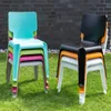 Stacked plastic chairs on a lawn in front of a brick wall. Produktbild-Vorschau