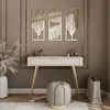 A stylish vanity table with a drawer and gold legs, adorned with decorative leaf wall art and a plush stool, set in a well-decorated room. Produktbild-Vorschau