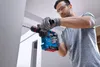 A man is using a cordless hammer drill to drill into a wall. Produktbild-Vorschau