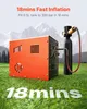 An orange and black air compressor connected to a black air tank, set on a grassy field with mountains in the background. Produktbild-Vorschau