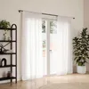 A room with a window covered by white curtains, a black bookshelf with decor, and a large potted plant. Náhľad obrázku produktu