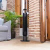 A tall black tower fan is placed on a rug next to a sofa and a potted plant in a room with brick walls and wooden shutters. Anteprima dell’immagine prodotto