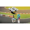 A LEGO Friends character holding a remote control for a drone, with a race track in the background. Podgląd zdjęcia produktu