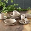 A set of stoneware dishes arranged on a wooden table with greenery in the background. Produktbild-Vorschau