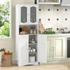 A white kitchen cabinet with glass doors and shelves, filled with jars and bread, stands next to a window and a kitchen counter. Produktbild-Vorschau