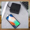 A black power strip is plugged into a white cable organizer, and a smartphone is charging from the power strip. Náhľad obrázku produktu