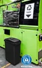 A black trash can lid is placed in front of a large green industrial machine. Voir les images du produit