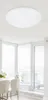 A white, round ceiling light fixture is mounted on a white ceiling above a dining area with large windows. Náhľad obrázku produktu