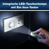 A hand holding a voltage tester near electrical outlets in a dark room. Voir les images du produit