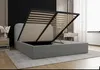 A bed with its storage compartment open, showing the slatted base and the interior storage space. The bed is in a bedroom setting with a nightstand and curtains visible in the background. Produktbild-Vorschau