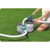 A person is kneeling on grass, operating a sand filter pump system for a swimming pool. Produktbild-Vorschau