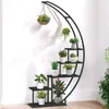 A black metal plant stand with multiple tiers, holding various potted plants, against a white wall. Produktbild-Vorschau