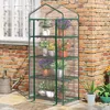 A greenhouse filled with plants is placed on a patio next to a brick wall and a window. Náhled obrázku produktu