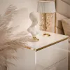 A white high-gloss nightstand with gold trim, featuring a decorative bust and a lamp. Produktbild-Vorschau